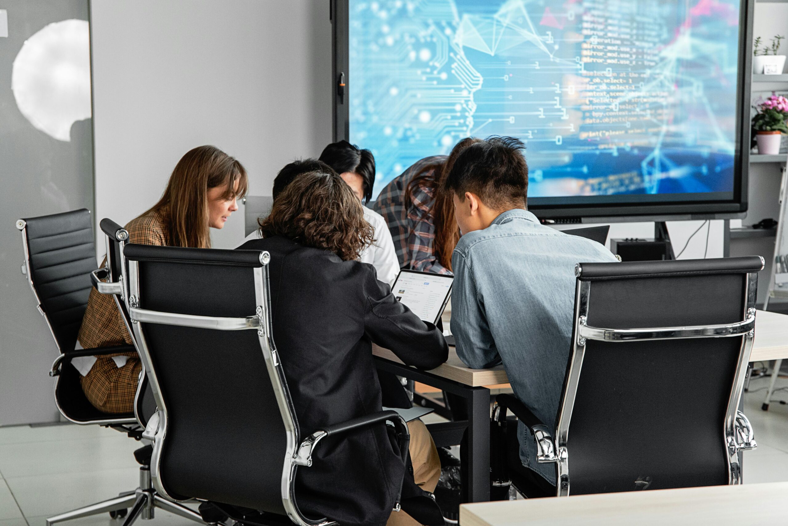 A diverse team collaborating in a modern office environment with a digital display.